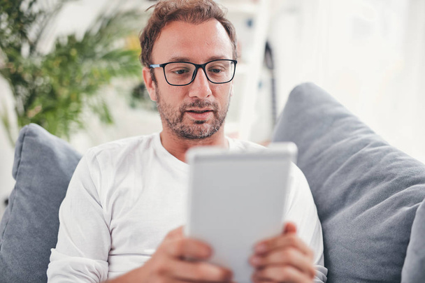 Homem usando tablet e sufring na internet em sua sala de estar
. - Foto, Imagem