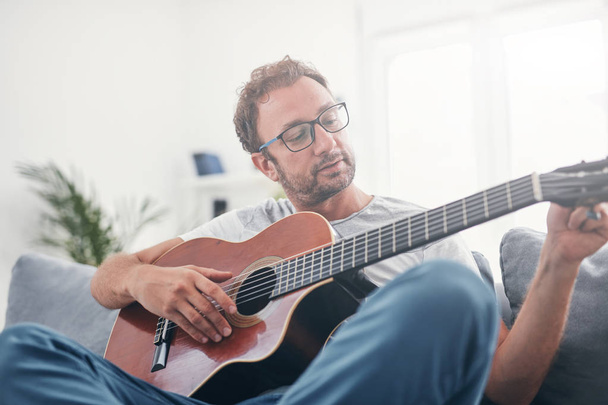 Mann spielt Akustikgitarre im Wohnzimmer. - Foto, Bild