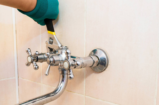 Рука в перчатке с гаечным ключом ремонтирует кран в ванной комнате
. - Фото, изображение