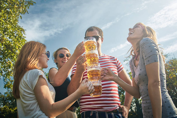 Группа молодых людей наслаждается и аплодирует пиву на открытом воздухе
. - Фото, изображение