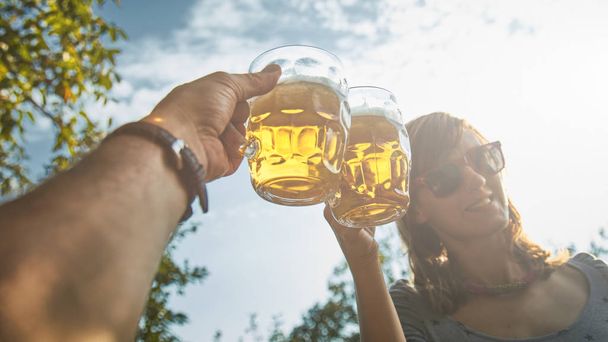 Pair holding beer glasses in the air from personal point of view - Foto, Imagen