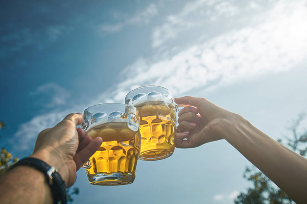 Pair holding beer glasses in the air from personal point of view - Photo, Image