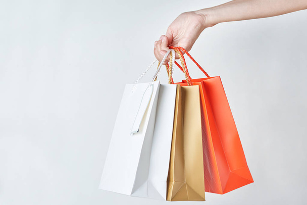 mão mulher segurar sacos de compras de papel colorido em um fundo branco, close-up
 - Foto, Imagem