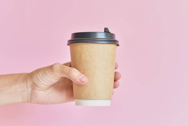 Макет жіночої руки, що тримає чашку кавового паперу на рожевому фоні
 - Фото, зображення