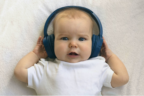 Criança bebê Criança feliz sorrindo em fones de ouvido azuis sem fio em um fundo branco. O conceito de tecnologia aprendendo desde o nascimento e música fina
 - Foto, Imagem