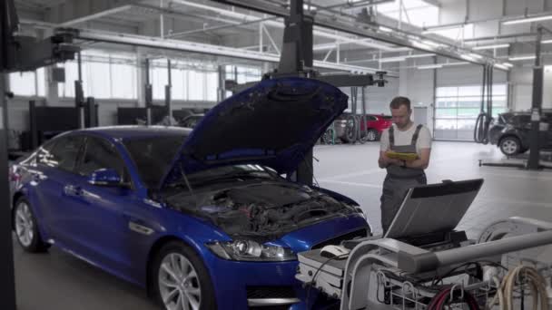 Olgun erkek mekanik notlar yapma ve bir araba tamir ederken bilgisayar kullanma - Video, Çekim