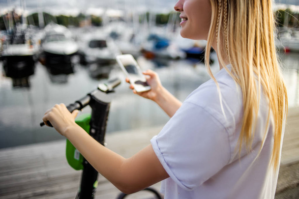 Femme utilisant des technologies électriques numériques modernes, prendre e-scooter en location dans la rue, tenant téléphone portable en utilisant l'application en ligne pour le libre-service. Electro transport, concept écologique
.  - Photo, image