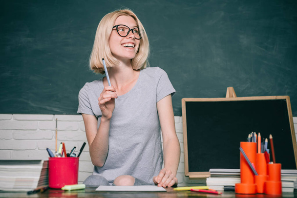Beautiful teacher in classroom. Portrait of Female University Student indoors. Teacher is skilled leader. Happy casual girl student with over blackboard background. - 写真・画像