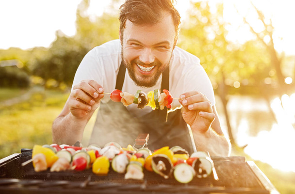 Cheerful chef cooking skewers on grill - Foto, afbeelding