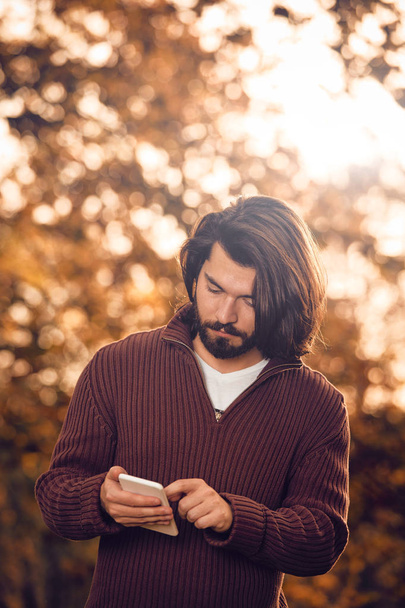 Сучасна людина використовує мобільний телефон в осінньому кольоровому парку
. - Фото, зображення