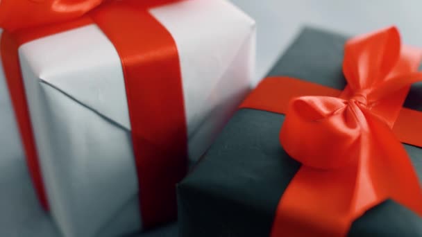 Fekete-fehér ajándékdoboz piros selyemszalaggal, fehér háttéren forgatva. Ajándékdoboz karácsonyra, fekete péntek és egyéb ünnepek. 4k felvételek bezárása. - Felvétel, videó