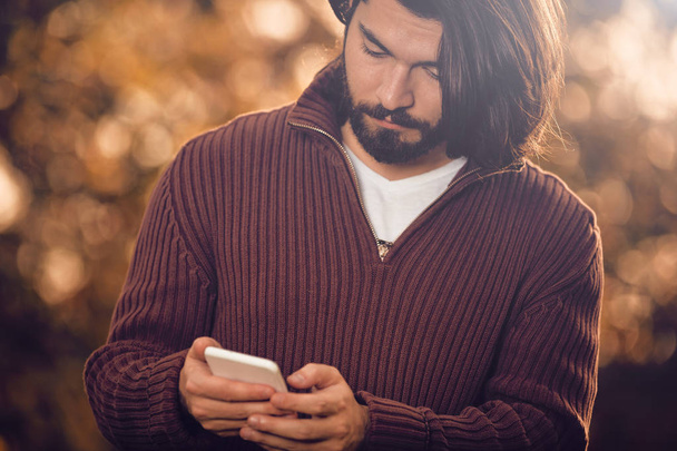 Moderní muž používající mobil v podzimním barevném parku. - Fotografie, Obrázek