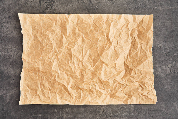 Crumpled piece of brown parchment or baking paper on black concr - Photo, image
