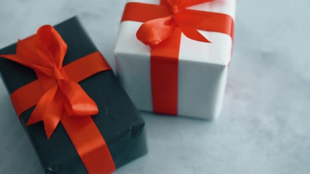 Zwart-wit geschenkdozen met rode satijnen lint roteren op grijze textuur oppervlak. Gift Box voor Kerstmis, Black Friday en andere feestdagen. 4k-beeldmateriaal close-up. - Video