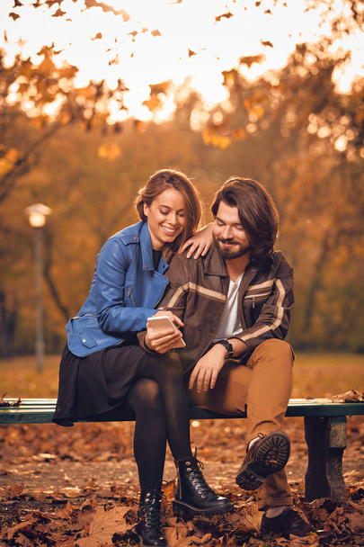 Young couple using cellphone in autumn colored park. - Photo, image