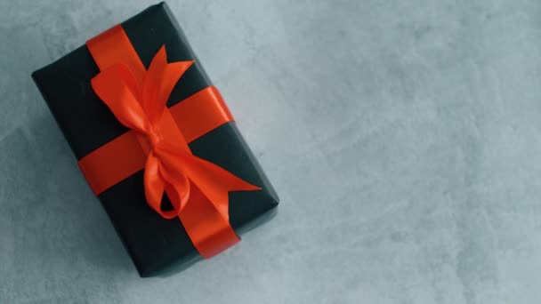 schwarzer Geschenkkarton mit rotem Seidenband, das sich auf der Texturoberfläche dreht. Geschenkbox für Weihnachten, Black Friday und andere Feiertage. Nahaufnahme 4k Filmmaterial. - Filmmaterial, Video