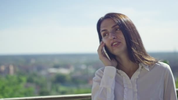 ηλιόλουστη μέρα, όμορφη μελαχρινή επιχείρηση γυναίκα μιλάει στο τηλέφωνο εναντίον του ορίζοντα - Πλάνα, βίντεο