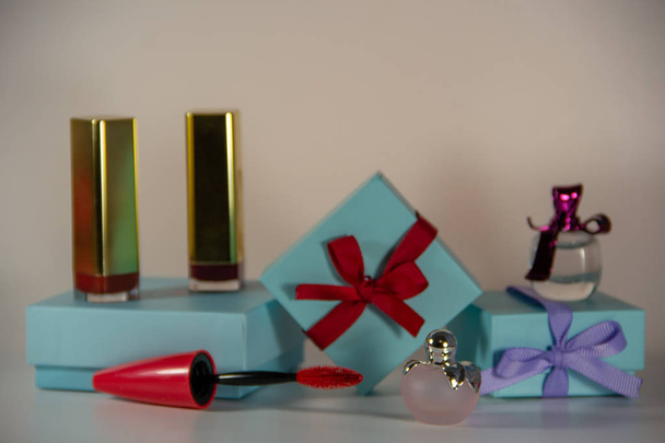 Blauwe gift Wrapping versierd met bogen, kleine flessen van vrouwelijke parfum, lippenstiften in goud kleur, een mascara borstel op een witte achtergrond. - Foto, afbeelding