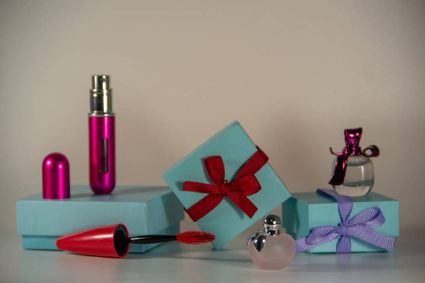 Envoltura de regalo azul decorada con arcos, pequeñas botellas de perfume femenino, cepillo de rímel sobre un fondo blanco
. - Foto, Imagen
