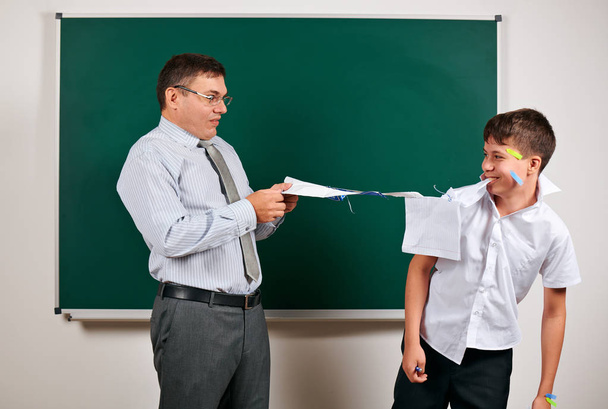 Portrait of a teacher and funny schoolboy with low discipline. Pupil very emotional, having fun and very happy, posing at blackboard background - back to school and education concept - Photo, Image