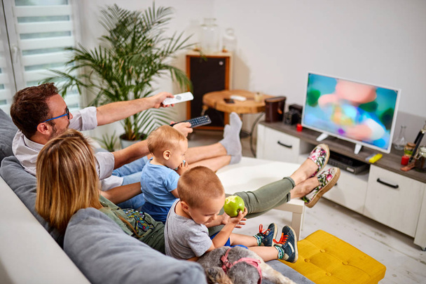 Young parents watching TV with baby boys. - Фото, изображение