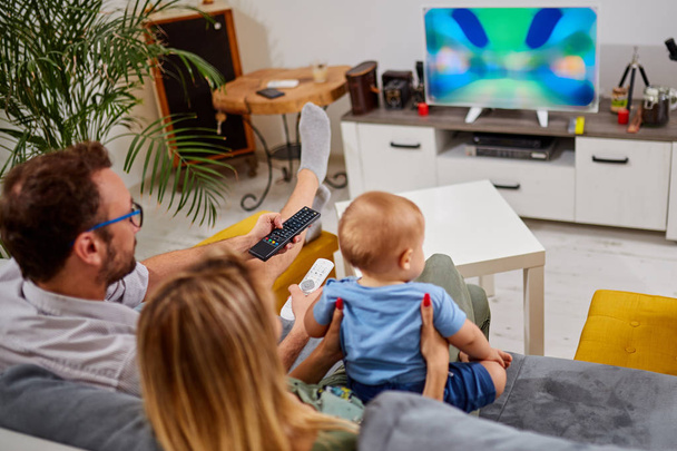 Young parents watching TV with baby boy. - Valokuva, kuva