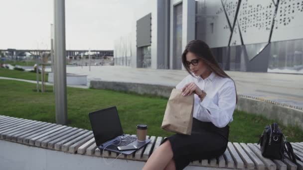 Mulher de negócios bem sucedida comer um croissant e beber café ao ar livre na hora do almoço
 - Filmagem, Vídeo