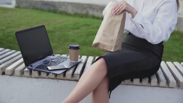 Mulher de negócios irreconhecível comer um croissant e beber café no parque
 - Filmagem, Vídeo