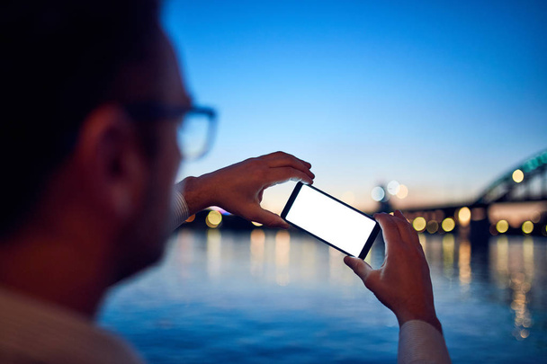 Uomo d'affari che utilizza il cellulare vicino al fiume con luci della città in b
 - Foto, immagini
