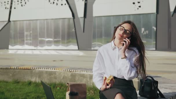 Mulher de negócios bonita comer um croissant enquanto fala no telefone celular e sorrindo ao ar livre
 - Filmagem, Vídeo