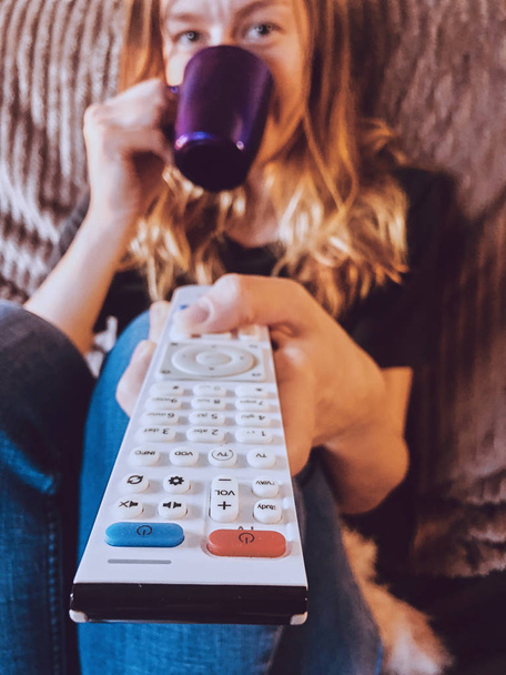 Жінка дивиться телевізор і п'є каву / чай на дивані
. - Фото, зображення