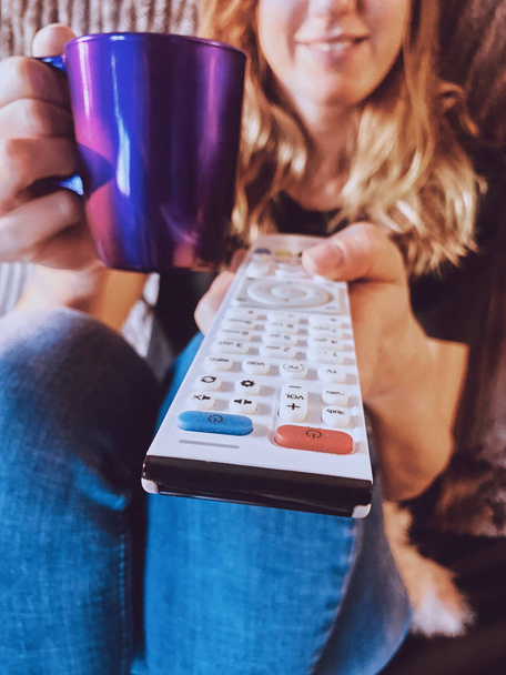 Woman watching TV and drinking coffee / tea on a couch. - Photo, Image