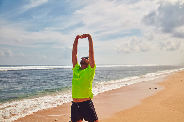 Sportsman stretching on a tropical sandy beach. - Fotoğraf, Görsel