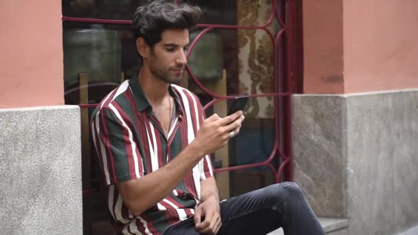 Молодий чоловік, використовуючи смартфон, сидить на міському кроці
. - Кадри, відео