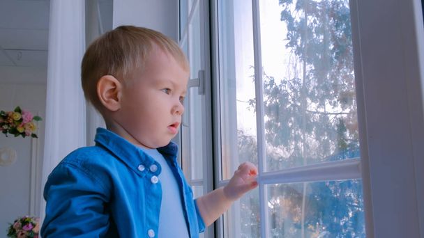 Страшный маленький мальчик смотрит в окно - Фото, изображение