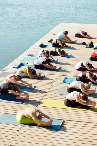 eine große Gruppe von Yoga-Teilnehmern auf einem Ponton in der Nähe des Sees. - Foto, Bild