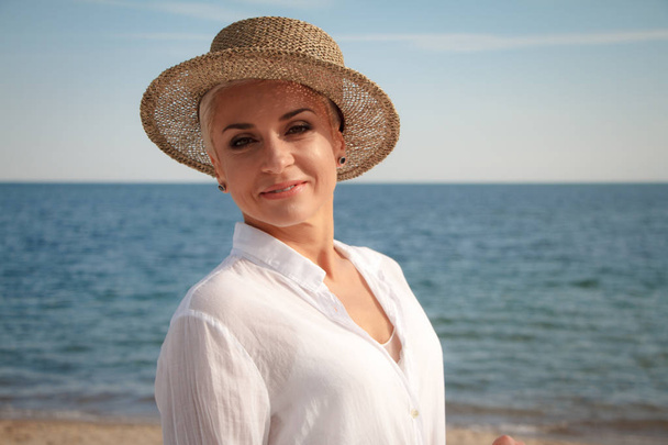 Urocza młoda kobieta z krótką fryzurą w kapelusz plażowy na plaży - Zdjęcie, obraz