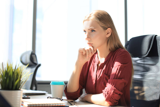 Geconcentreerde moderne vrouw houdt de hand op de kin en denkt over zaken terwijl ze op kantoor werkt - Foto, afbeelding