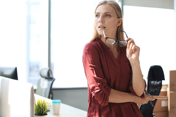 Attractive business woman is looking in the window and holding holding her glasses while standing in the office - Foto, afbeelding
