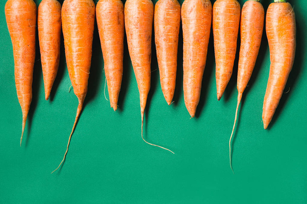 varias zanahorias frescas se encuentran en una fila sobre un fondo verde
. - Foto, imagen