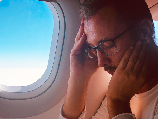 Κουρασμένος/άρρωστος επιβάτης σε ένα μοντέρνο κάθισμα αεροπλάνου δίπλα στη νίκη - Φωτογραφία, εικόνα