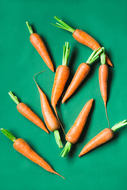 varias zanahorias frescas se encuentran en una fila sobre un fondo verde
. - Foto, imagen