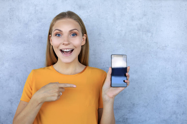Портрет улыбающейся девушки с пустым экраном мобильного телефона, изолированного на сером фоне
 - Фото, изображение