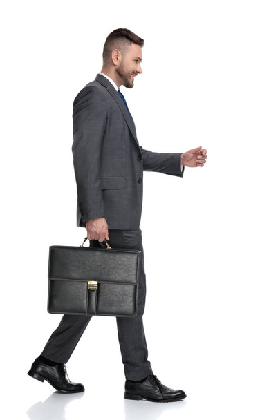 スーツケースを持って歩く幸せな若いビジネスマンの側面図 - 写真・画像