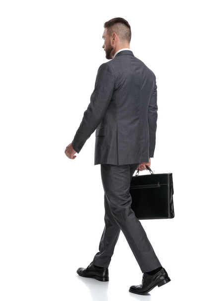 vista lateral trasera de un hombre de negocios caminando sosteniendo un maletín
  - Foto, Imagen