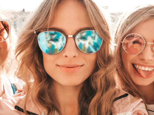 Tres jóvenes mujeres hipster sonrientes en ropa de verano.Chicas tomando fotos de autorretrato de selfie en el teléfono inteligente.Modelos posando en la calle.Mujer mostrando emociones positivas en la cara en gafas de sol
 - Foto, imagen