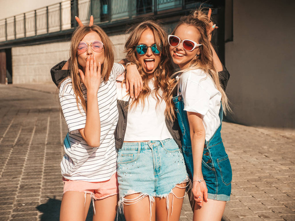 Portrait of three young beautiful smiling hipster girls in trendy summer clothes. Sexy carefree women posing the street.Positive models having fun in sunglasses.Hugging and showing tongue - Foto, Imagem