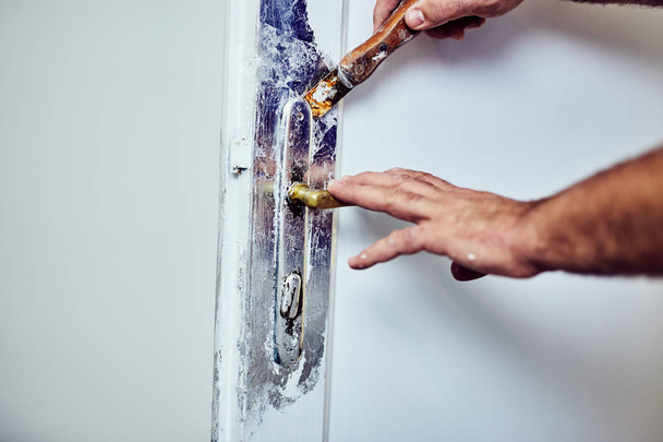 Handyman za pomocą dłuta wokół drzwi Lock TTO peeling starej farby. - Zdjęcie, obraz