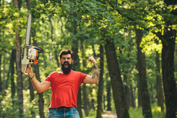 Woodcutter with axe or chainsaw in the summer forest. Lumberjack worker standing in the forest with chainsaw. - Fotoğraf, Görsel