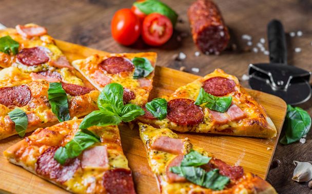 Pfefferoni-Pizza mit Mozzarella, Salami, Schinken, Gewürzen und frischem Basilikum. italienische Pizza auf Holztischhintergrund - Foto, Bild